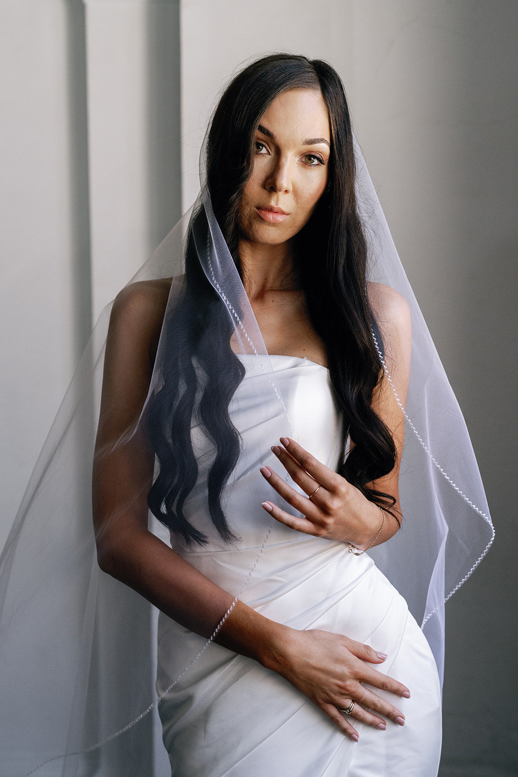 Woman in a white dress with a veil against a neutral background