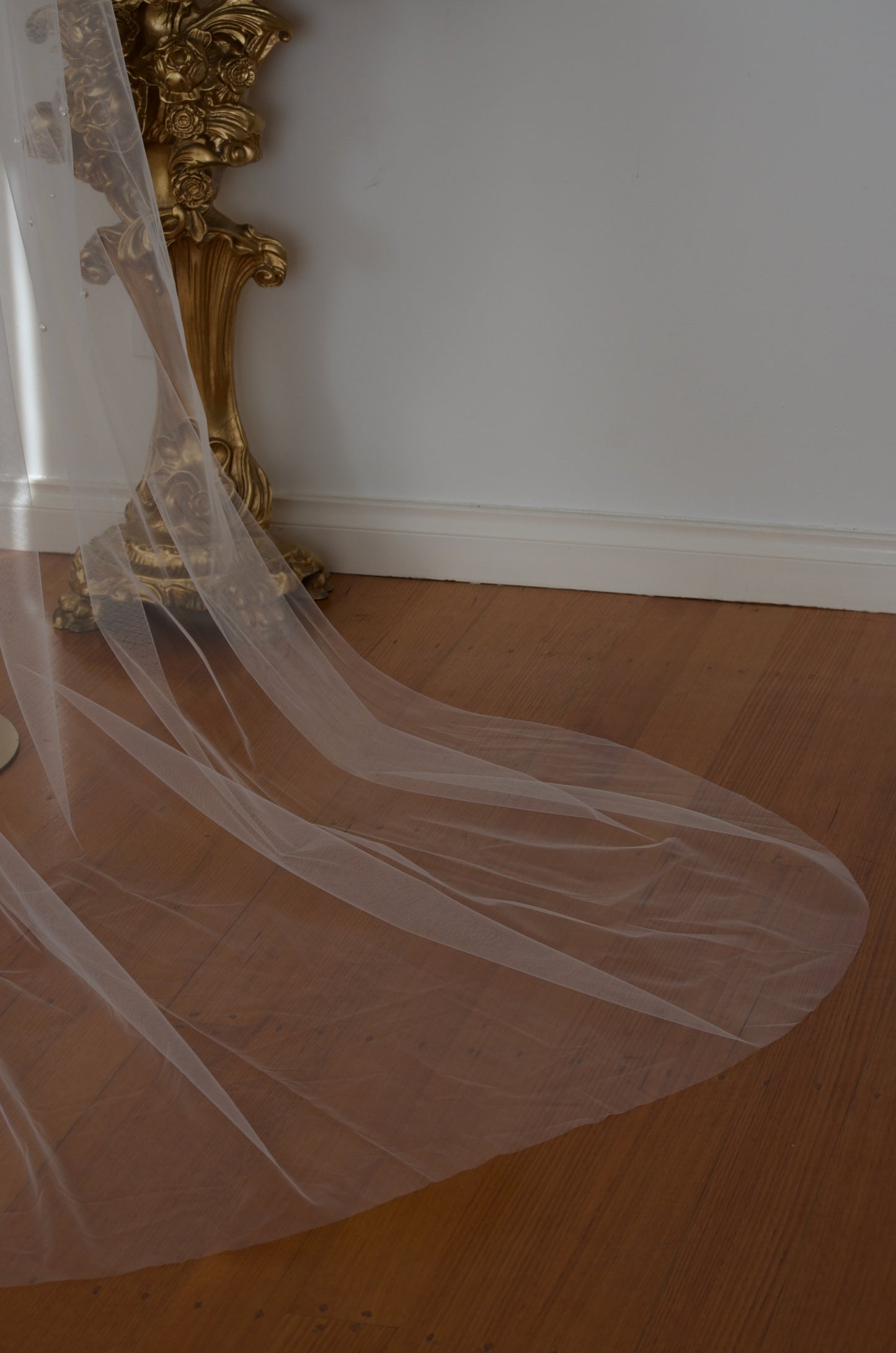 White wedding veil on a wooden floor with a gold decorative object in the background.