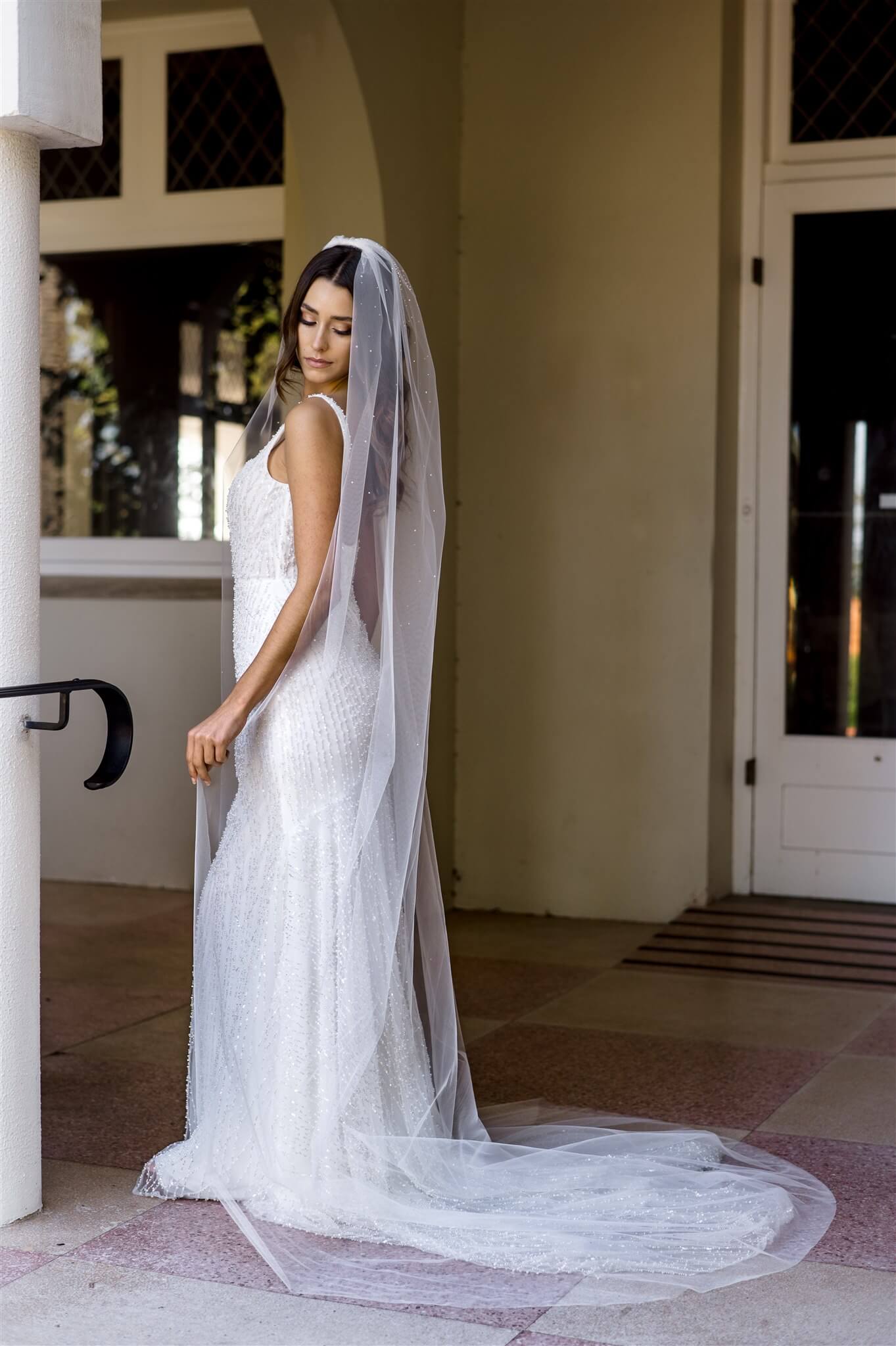 Bride in a white wedding dress with a long veil standing in front of a building entrance.