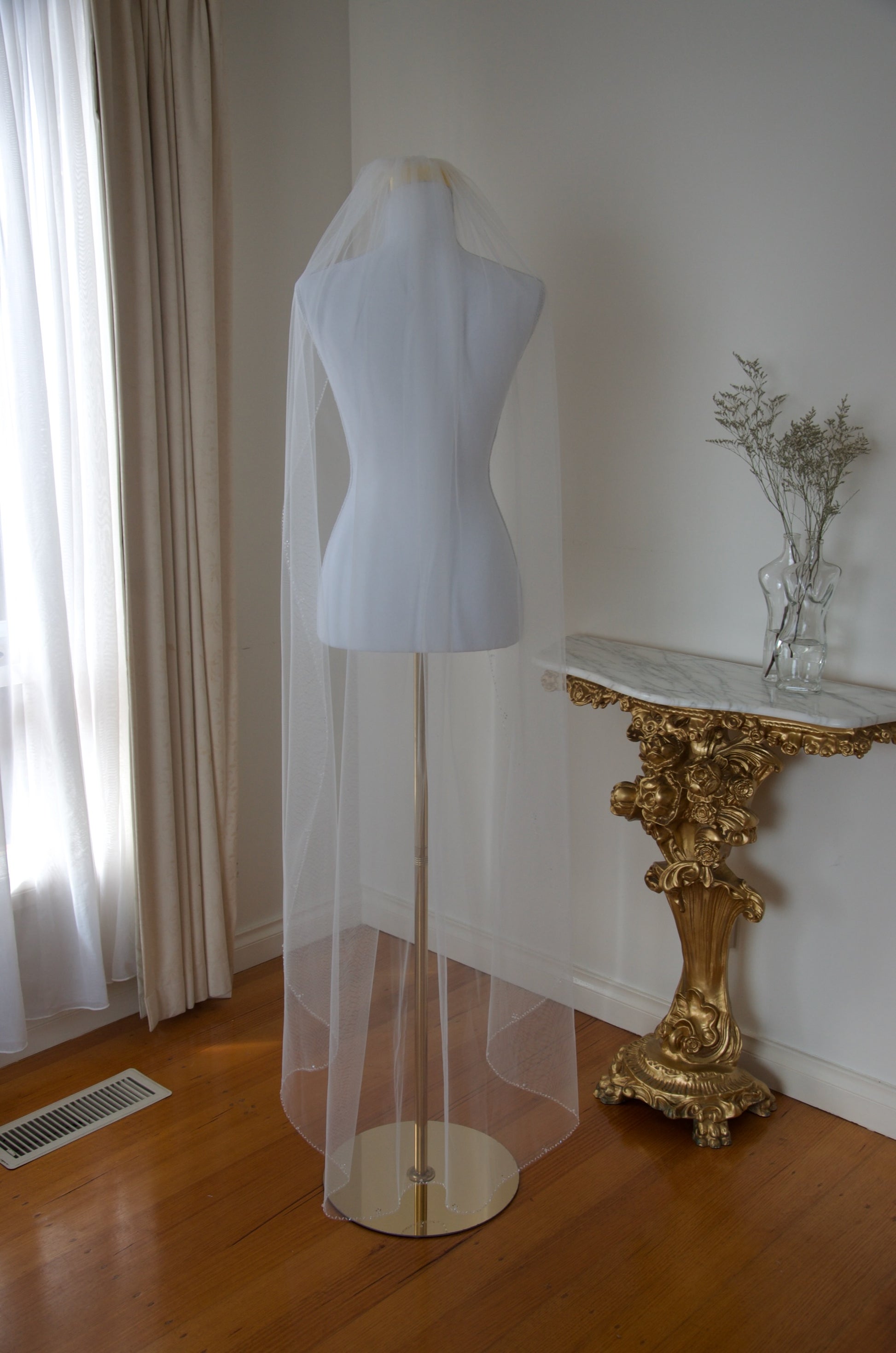 Mannequin wearing a white veil in a room with a gold table and curtains.