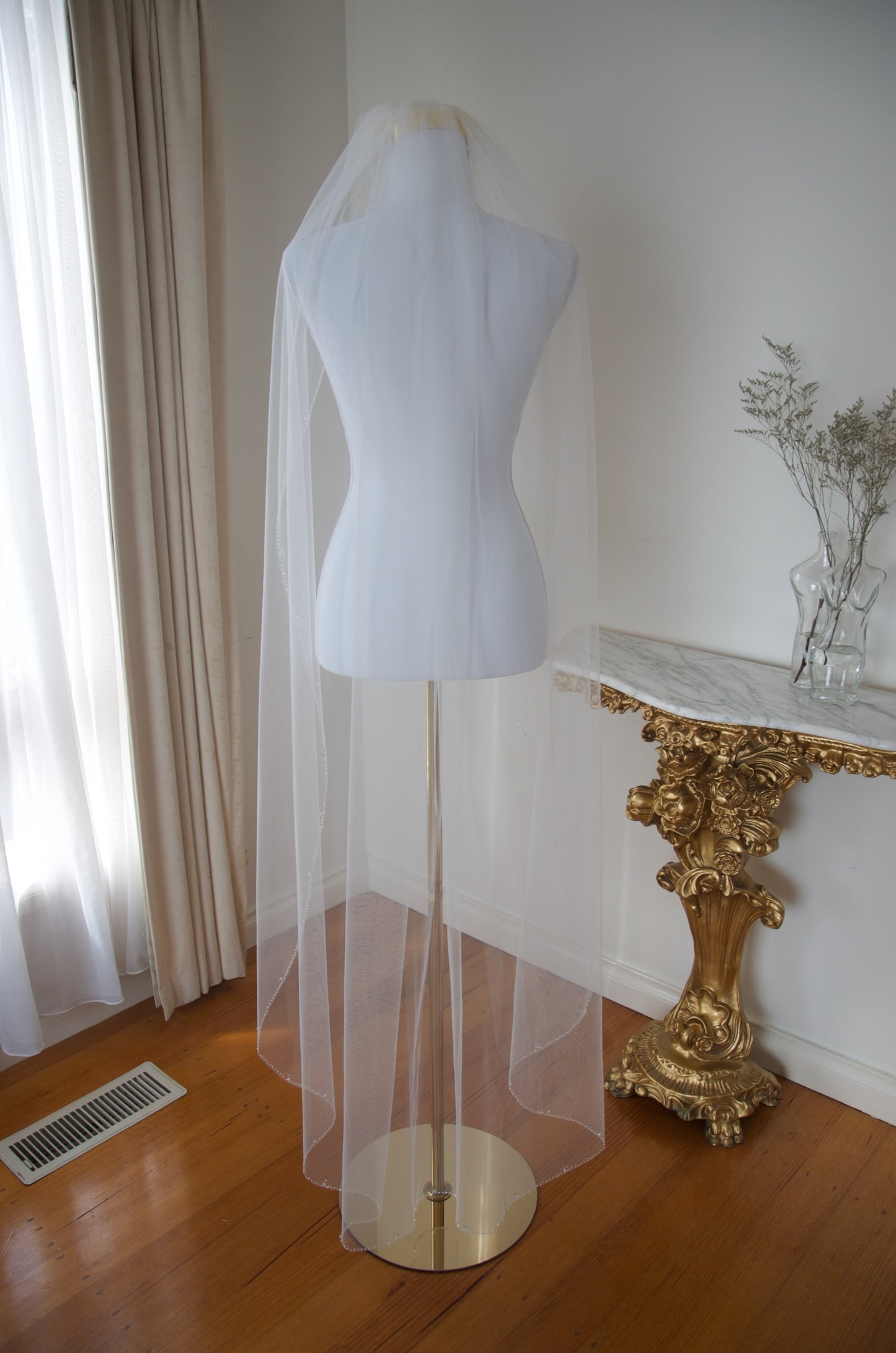 Mannequin wearing a white veil in a room with a gold console table and white curtains.
