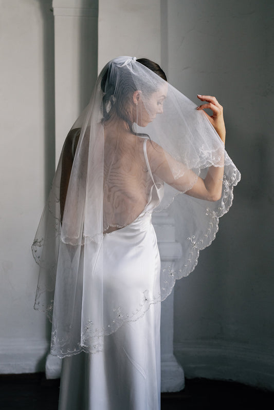 Woman wearing a white wedding dress with a sheer veil against a plain background