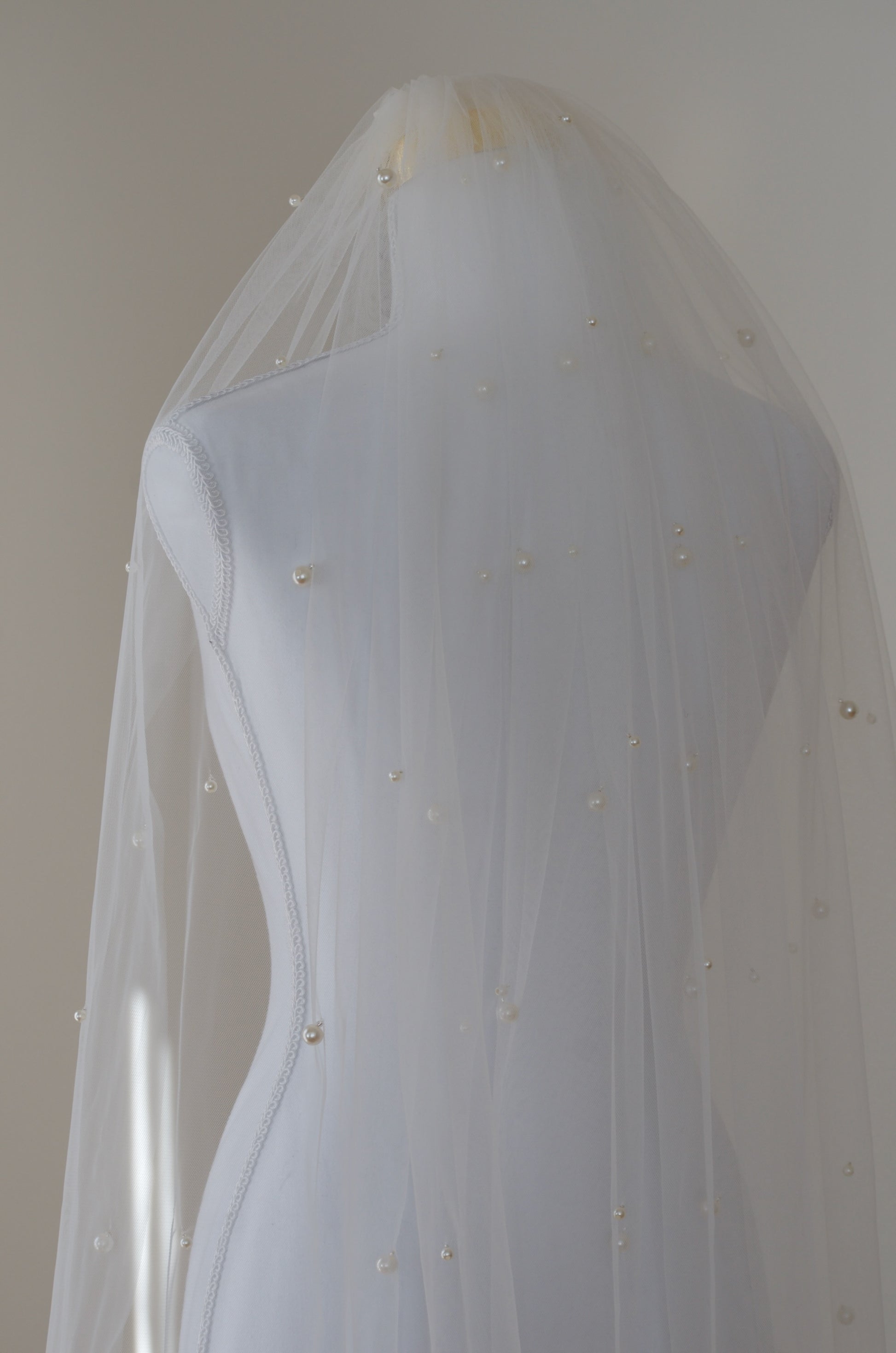 White wedding veil with small embellishments on a mannequin against a plain background